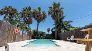 A backyard with a swimming pool, wooden fence, and palm trees. - New 3BR Townhome, Heated Pool, Beach Steps SPI (South Padre Island)