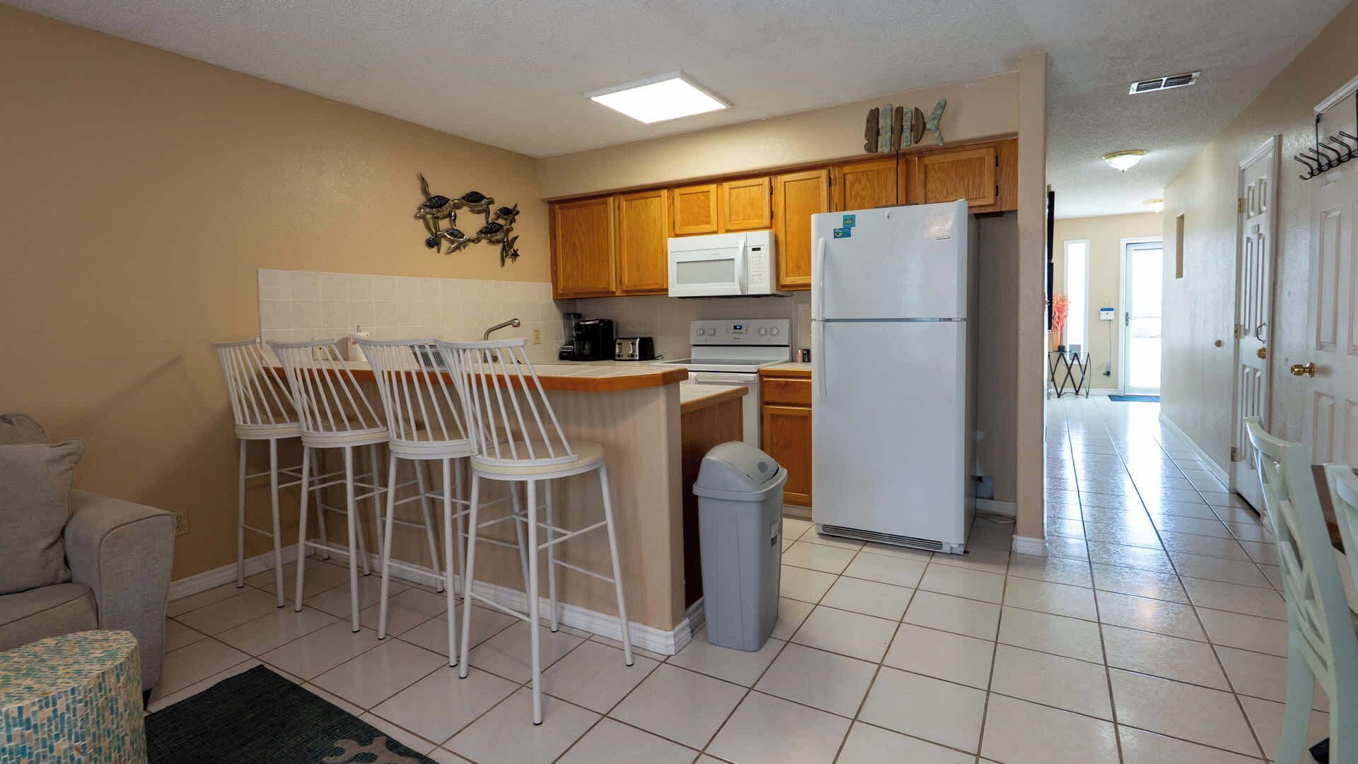 A kitchen with a central island, white chairs, a refrigerator, and wooden cabinets.