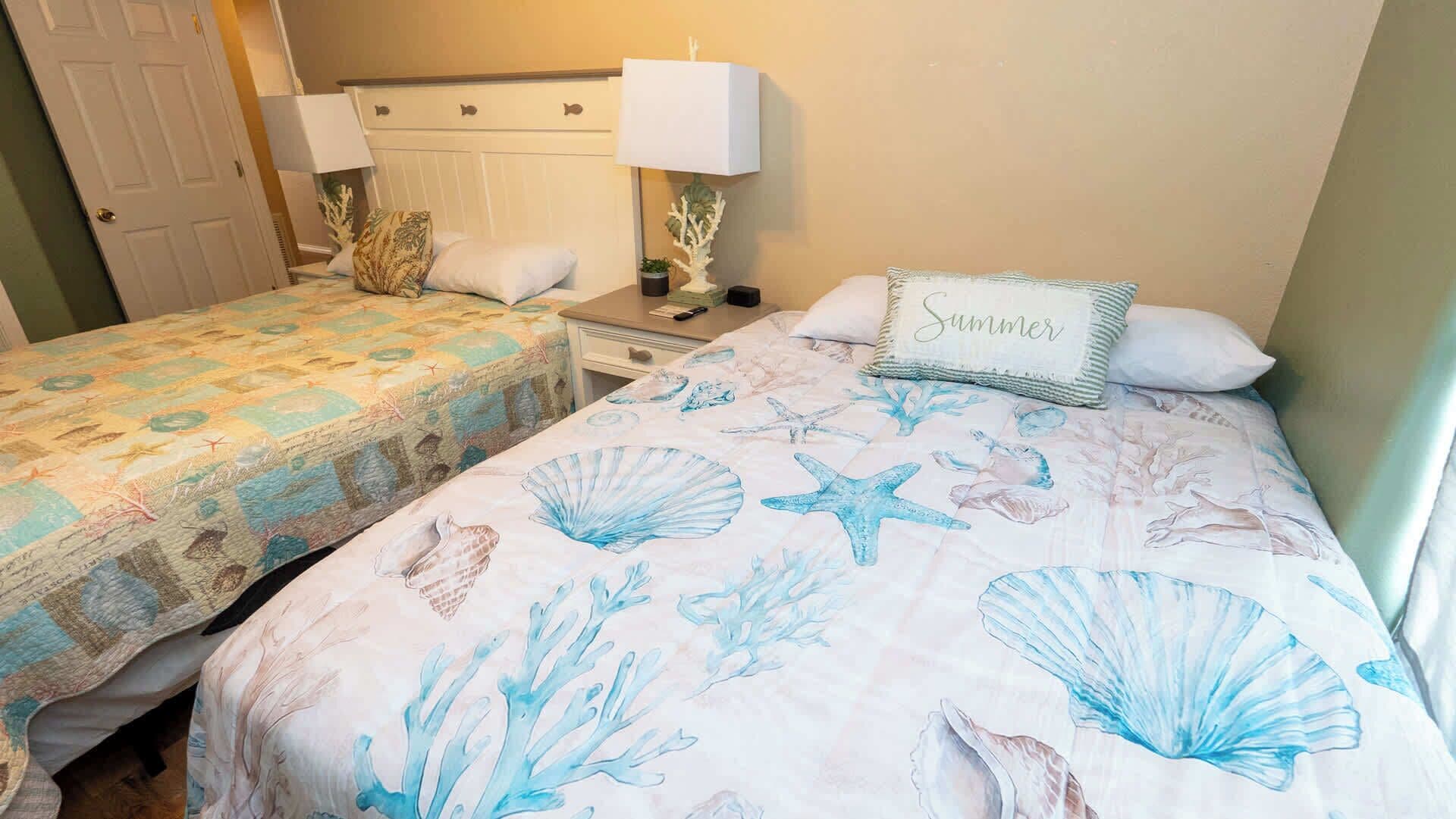 Deux chambres adjacentes, décorées sur le thème de la mer, avec une table de chevet et une lampe, ainsi qu’une porte.