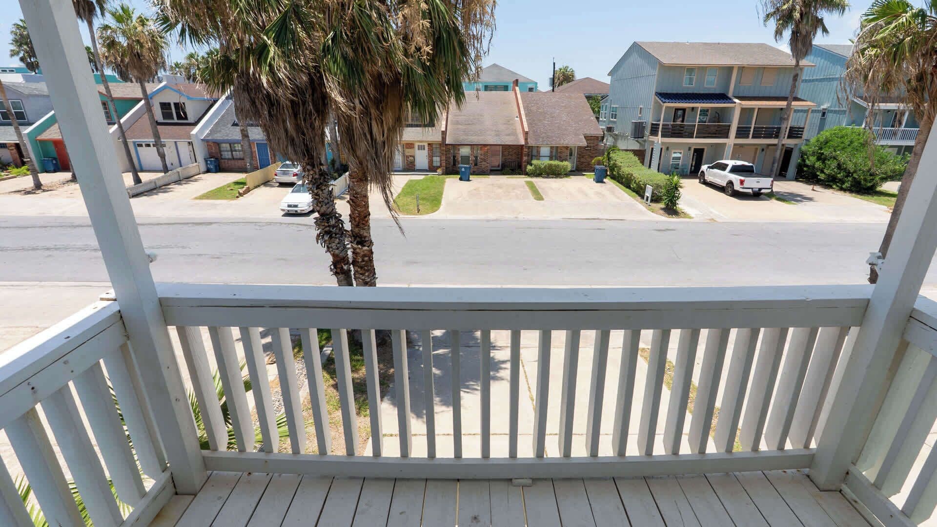 A residential area with a white wooden porch, houses with various architectural styles, and a clear sky.