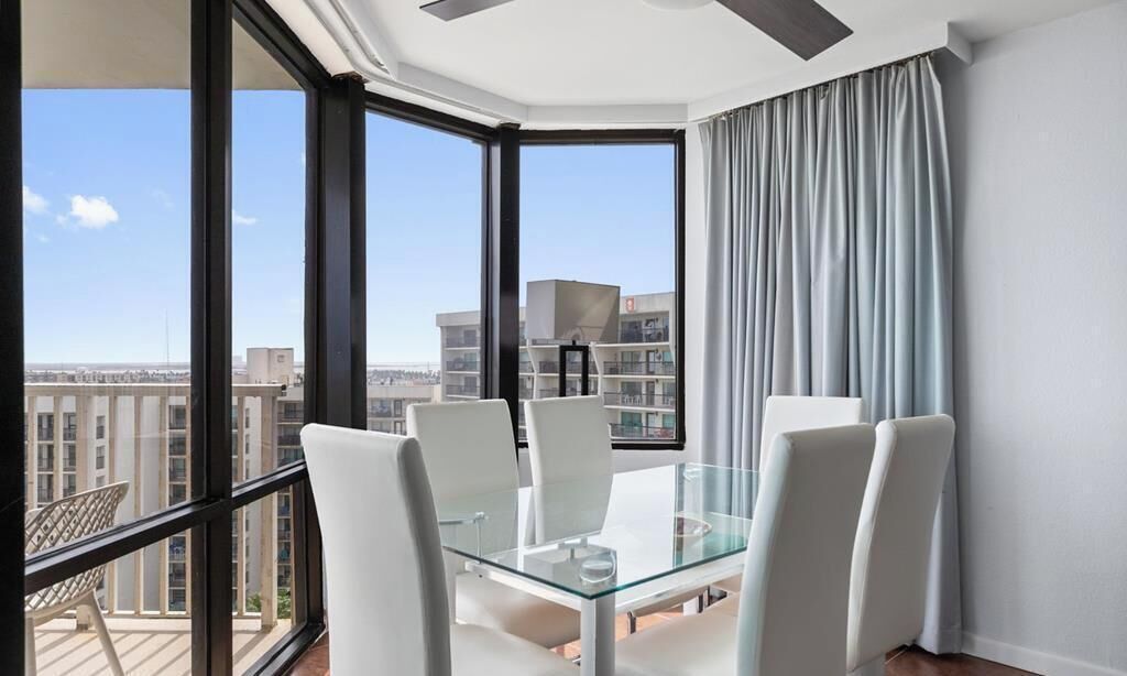 A modern room with a glass table and chairs, large windows, and a view of the cityscape.