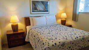 A hotel room with a bed, two bedside tables with lamps, a nightstand with a drawer, a framed picture on the wall, and a window with curtains. - 2BR Half Block to Beach, Pool Hot Tub Patio SPI (South Padre Island)
