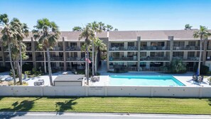 A multi-story hotel with a swimming pool, palm trees, and outdoor seating areas. - 2BR Half Block to Beach, Pool Hot Tub Patio SPI (South Padre Island)