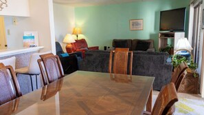 A living room with a dining table, chairs, sofas, a TV, and a lamp. - 2BR Half Block to Beach, Pool Hot Tub Patio SPI (South Padre Island)