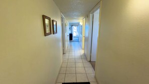 A narrow hallway with white walls and a tiled floor, leading to a door at the end. - 2BR Half Block to Beach, Pool Hot Tub Patio SPI (South Padre Island)