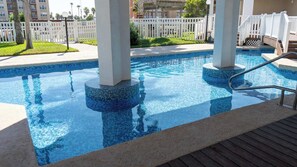 Una piscina con borde de azulejos, rodeada por una cubierta de madera y barandillas blancas.