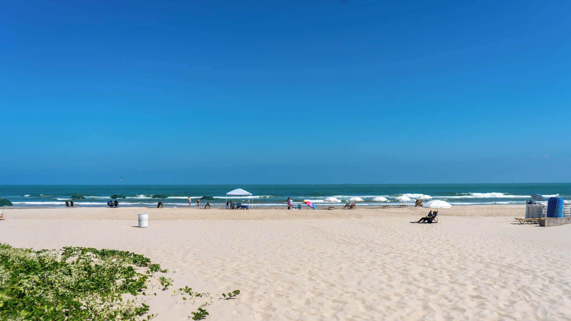 A beach with umbrellas, lounge chairs, and a clear sky.