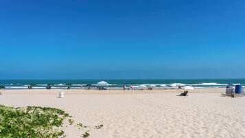 A beach with umbrellas, lounge chairs, and a clear sky.