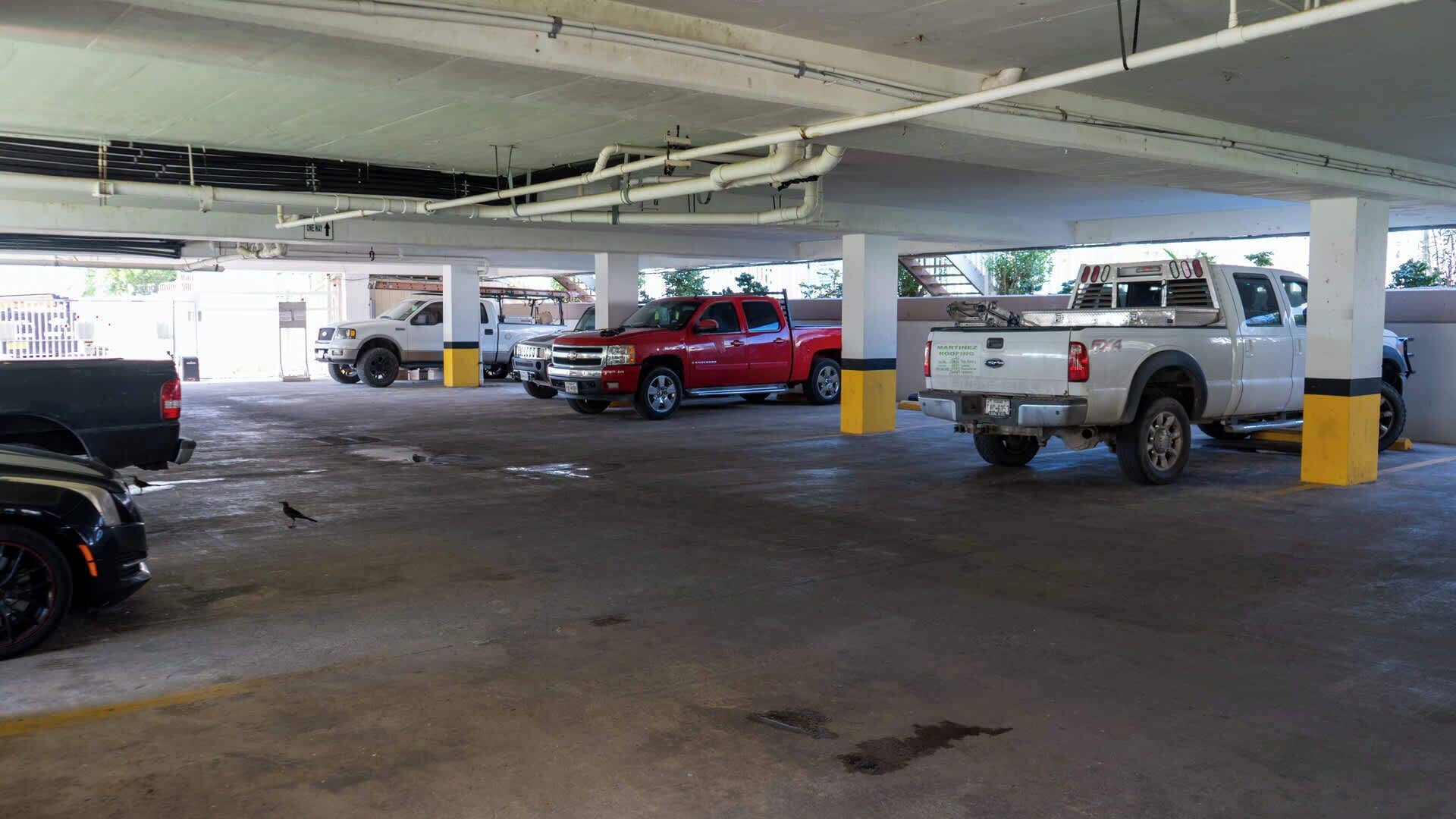 Un estacionamiento de varios niveles con varios vehículos estacionados, incluyendo una camioneta roja y una camioneta blanca.