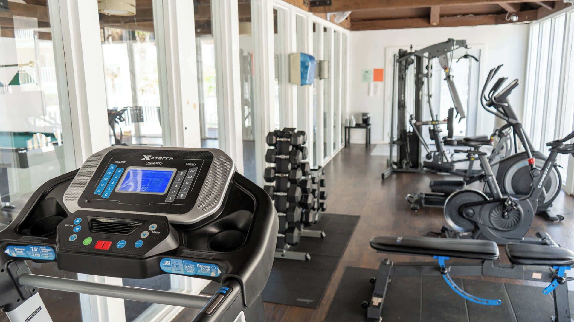 A gym with a treadmill, dumbbells, and stationary bikes.