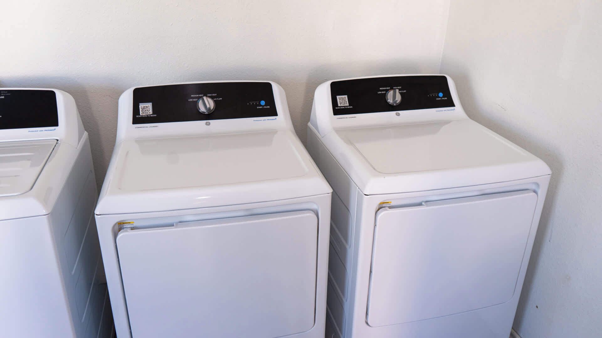 Three white front-loading washing machines lined up against a white wall.