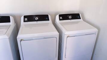 Three white front-loading washing machines lined up against a white wall.