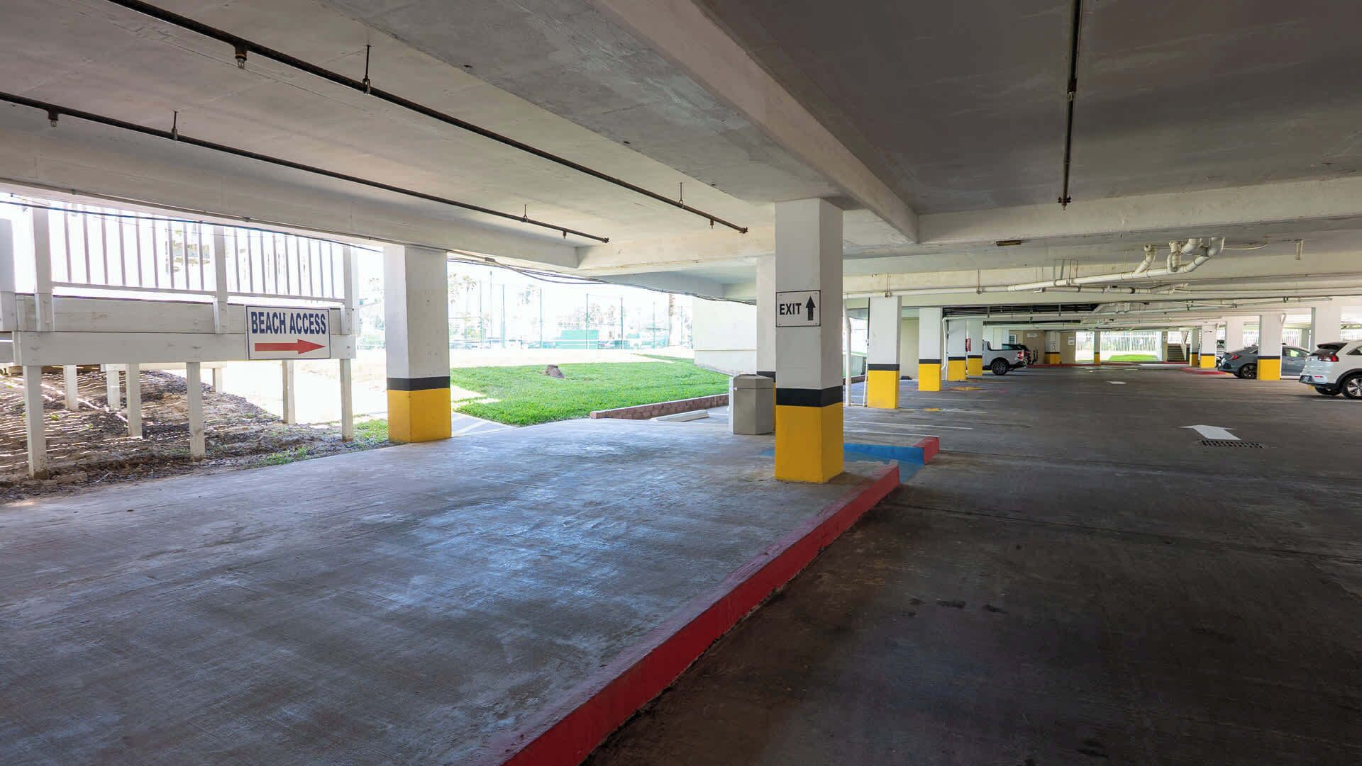Een ondergrondse parkeergarage met betonnen pilaren, duidelijke borden met 'STRANDTOEGANG' en een 'UITGANG' bord.