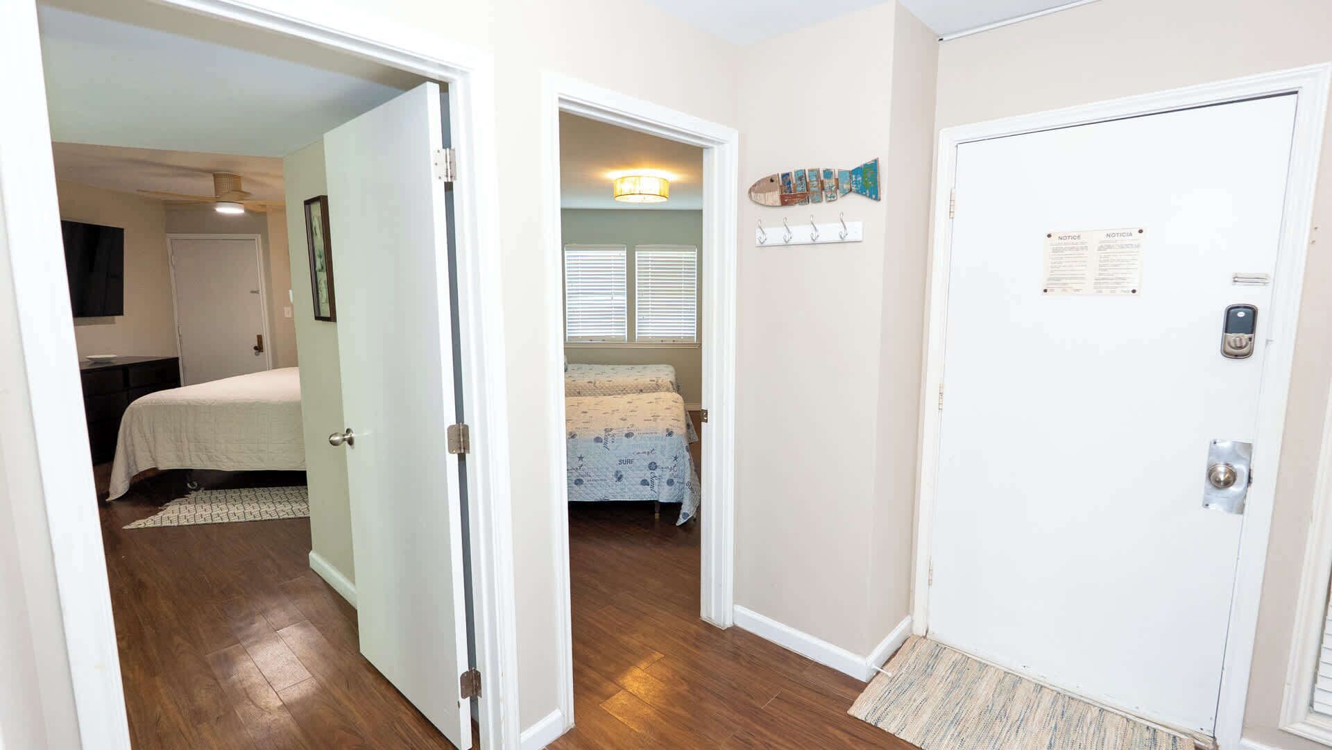 A hallway with a door leading to a bedroom with a bed and a window with blinds.