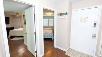 A hallway with a door leading to a bedroom with a bed and a window with blinds.