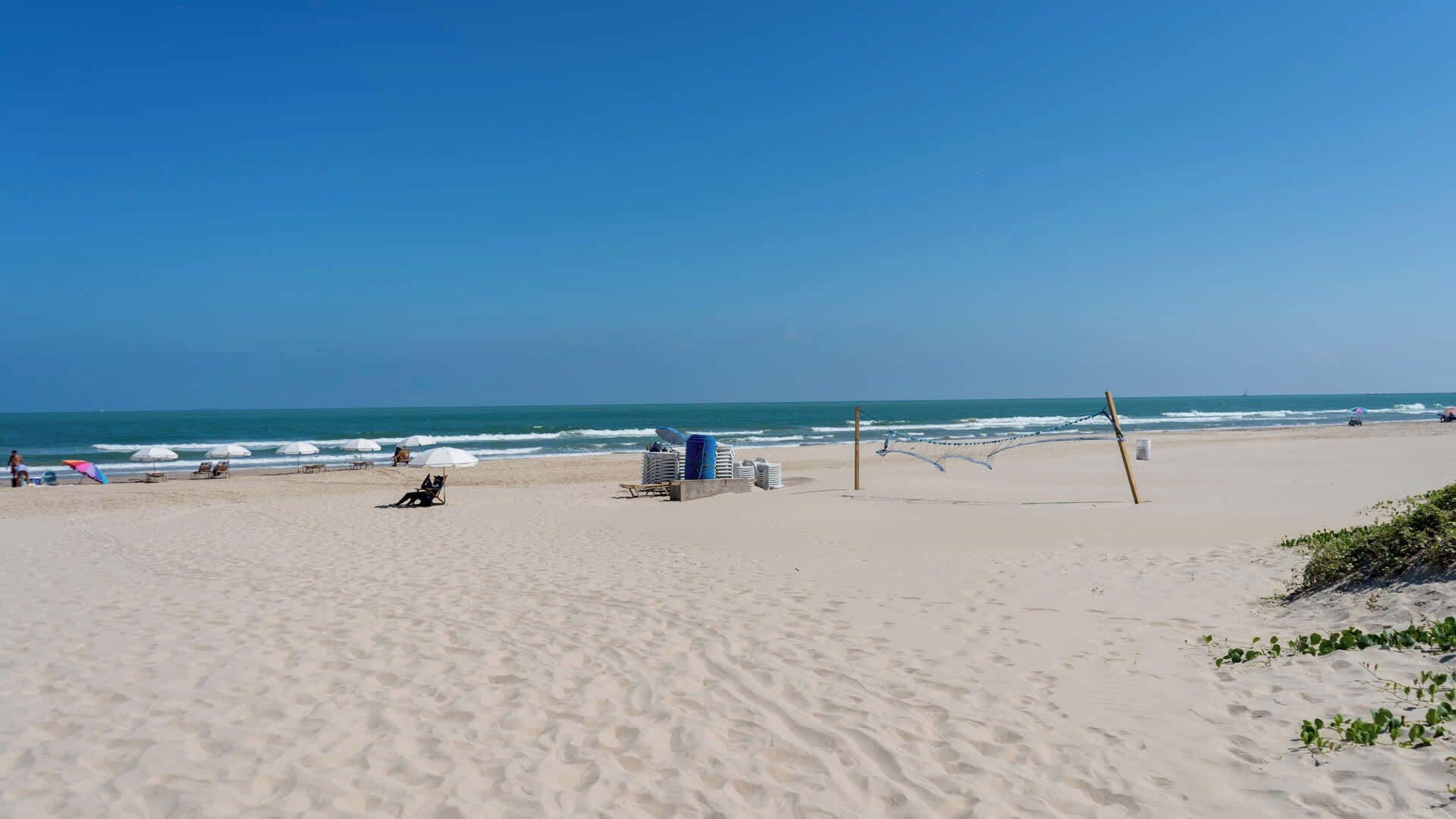 Une plage avec un filet de volley-ball, des parasols et un poste de surveillance pour les sauveteurs.