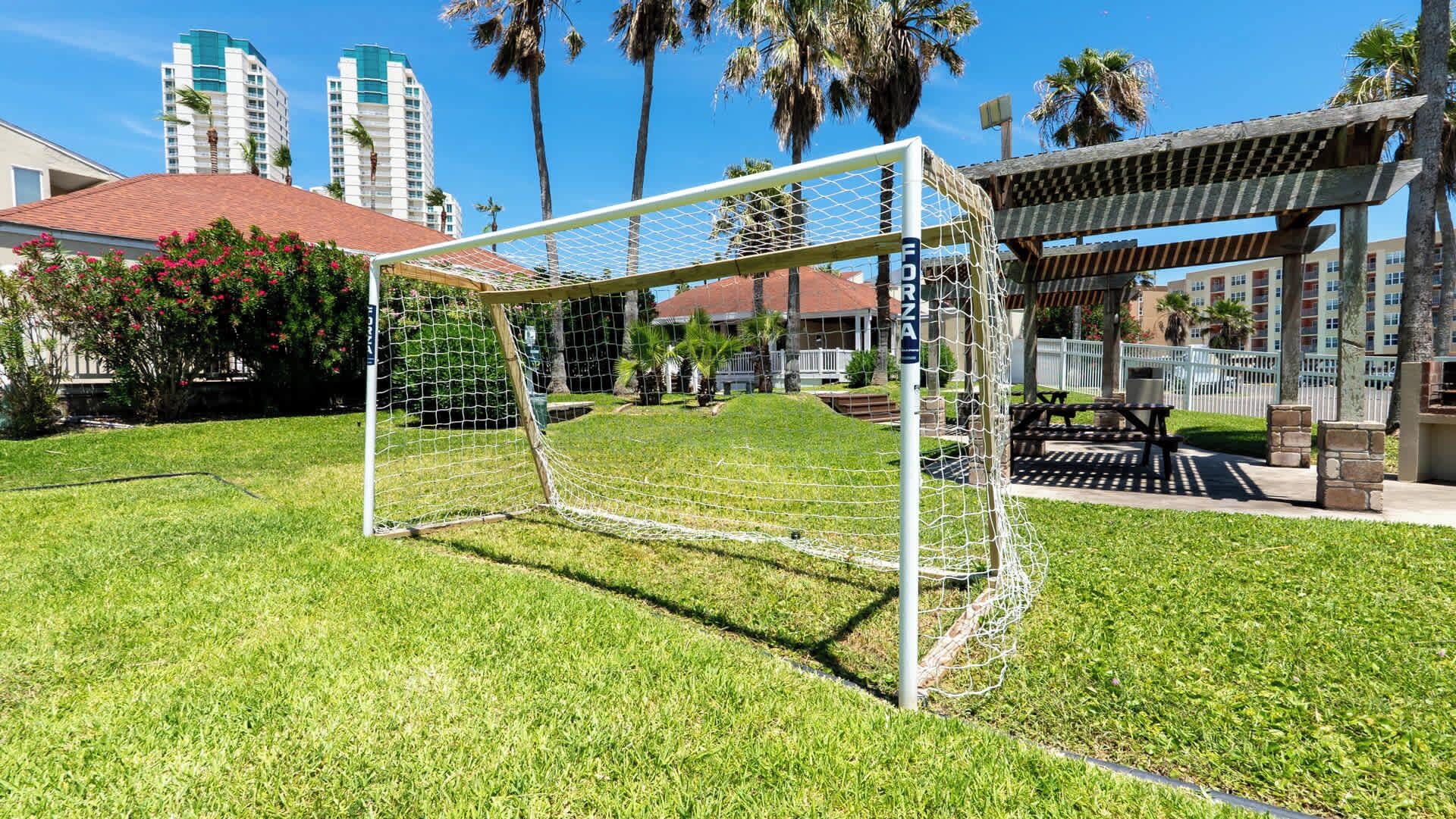 A soccer goal in a well-maintained grassy area with a wooden pergola and a barbecue area in the background.