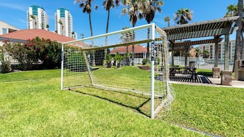 A soccer goal in a well-maintained grassy area with a wooden pergola and a barbecue area in the background.