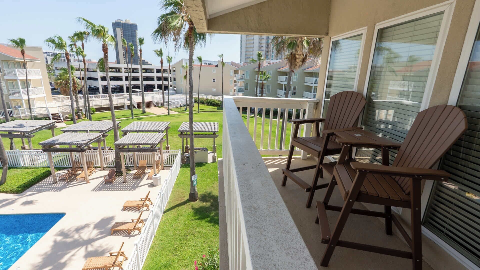 A balcony with outdoor furniture, a swimming pool, and a view of surrounding buildings.