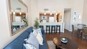 A modern living room with a sofa, a dining table, and a kitchen in the background. - Family Condo - Pool, Jacuzzi & BBQ - Walk to Beach (South Padre Island)