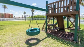 Un parque infantil con columpios, un neumático colgante y una mesa de picnic.
