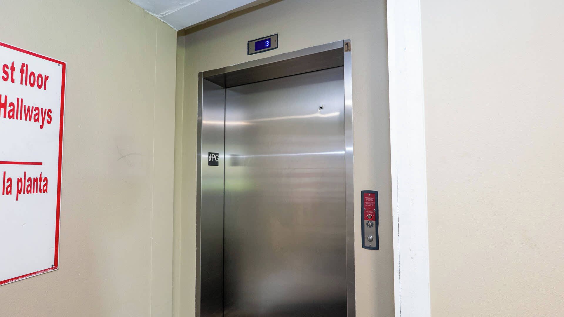 An elevator with a digital display, a fire alarm button, and a sign indicating the location of the first floor hallways and the plant.