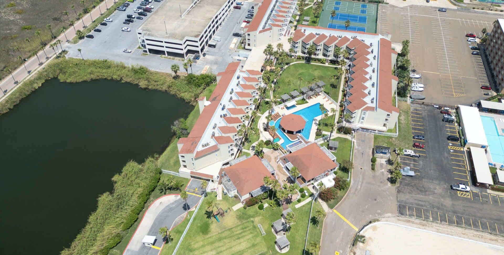 Luchtbeeld van een resort met een zwembad, parkeerplaatsen en een waterlichaam.