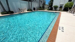Ein rechteckiger Swimmingpool mit klarem, blauem Wasser, umgeben von einer weißen Wand und einer gefliesten Liegefläche.