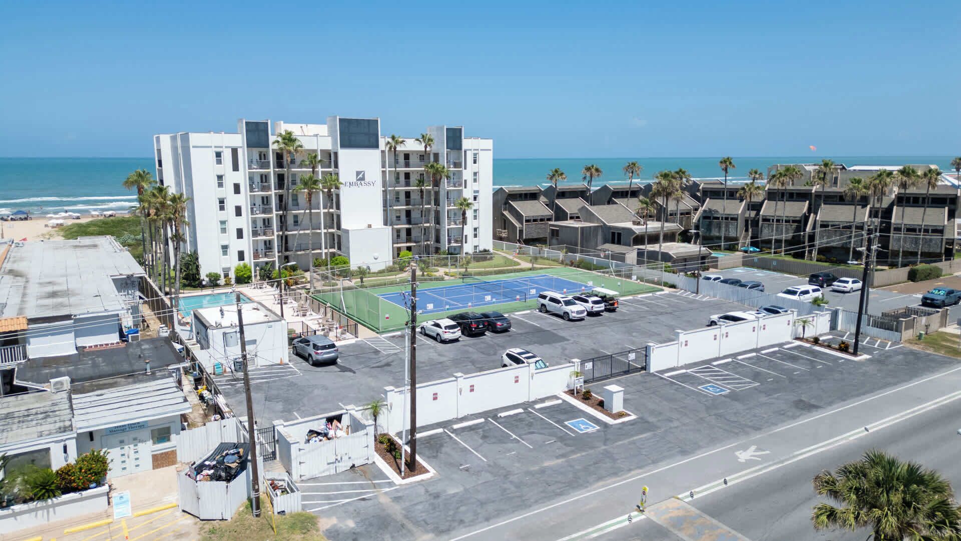 A multi-story hotel with a rooftop pool, tennis courts, and a parking lot.