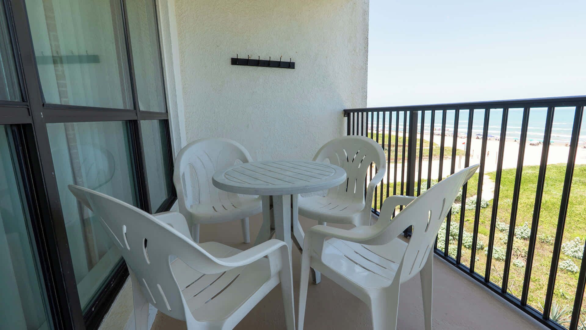 Een balkon met een tafel en stoelen, uitzicht op het strand, en een metalen hekwerk.