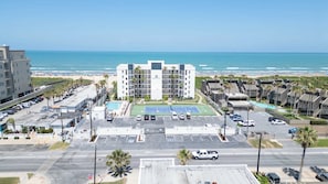 A multi-story hotel with a tennis court, parking lot, and ocean view. - Beachfront 2br, 5th Floor Views, Walkable SPI (South Padre Island)