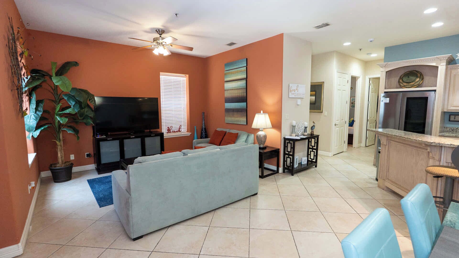 A living room with a sofa, TV, ceiling fan, and a dining area with chairs and a table.