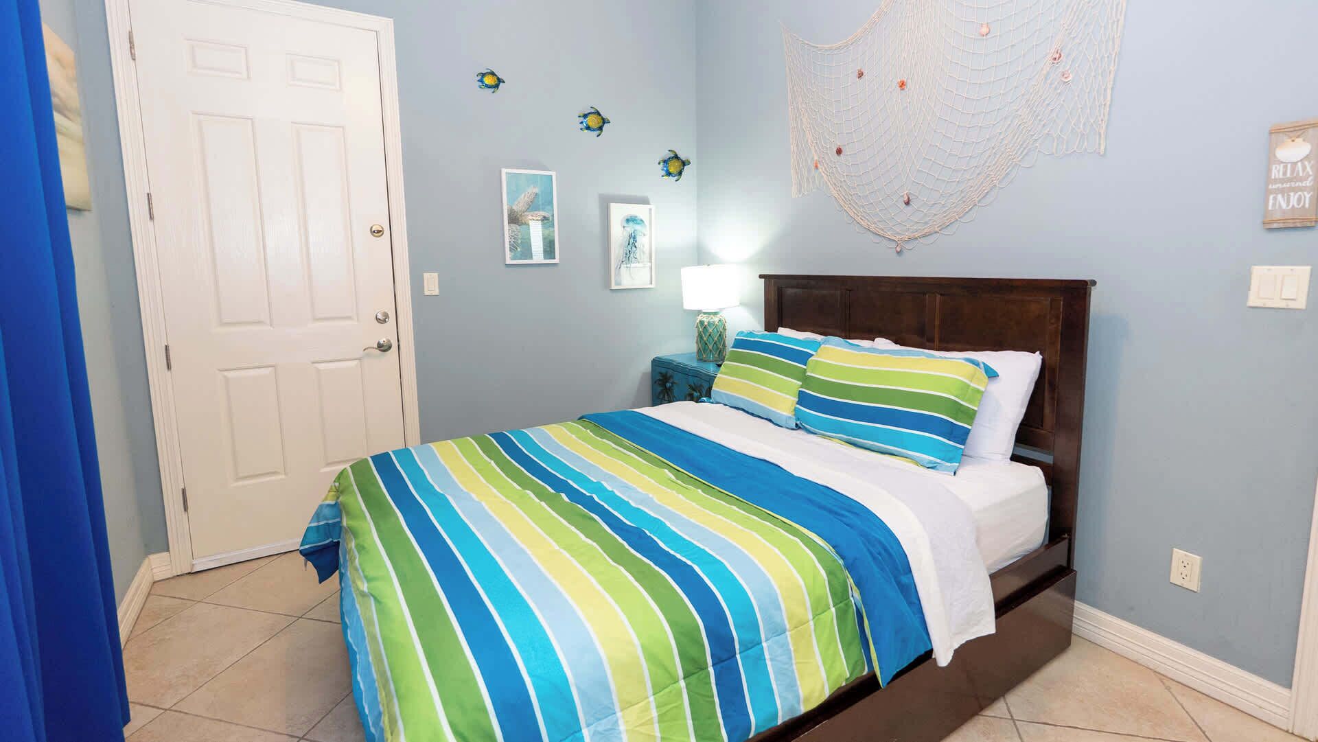 Une chambre à coucher avec une couvre-lit à rayures, une tête de lit en bois, une porte blanche et des éléments de décoration murale, notamment un filet et des tableaux encadrés.