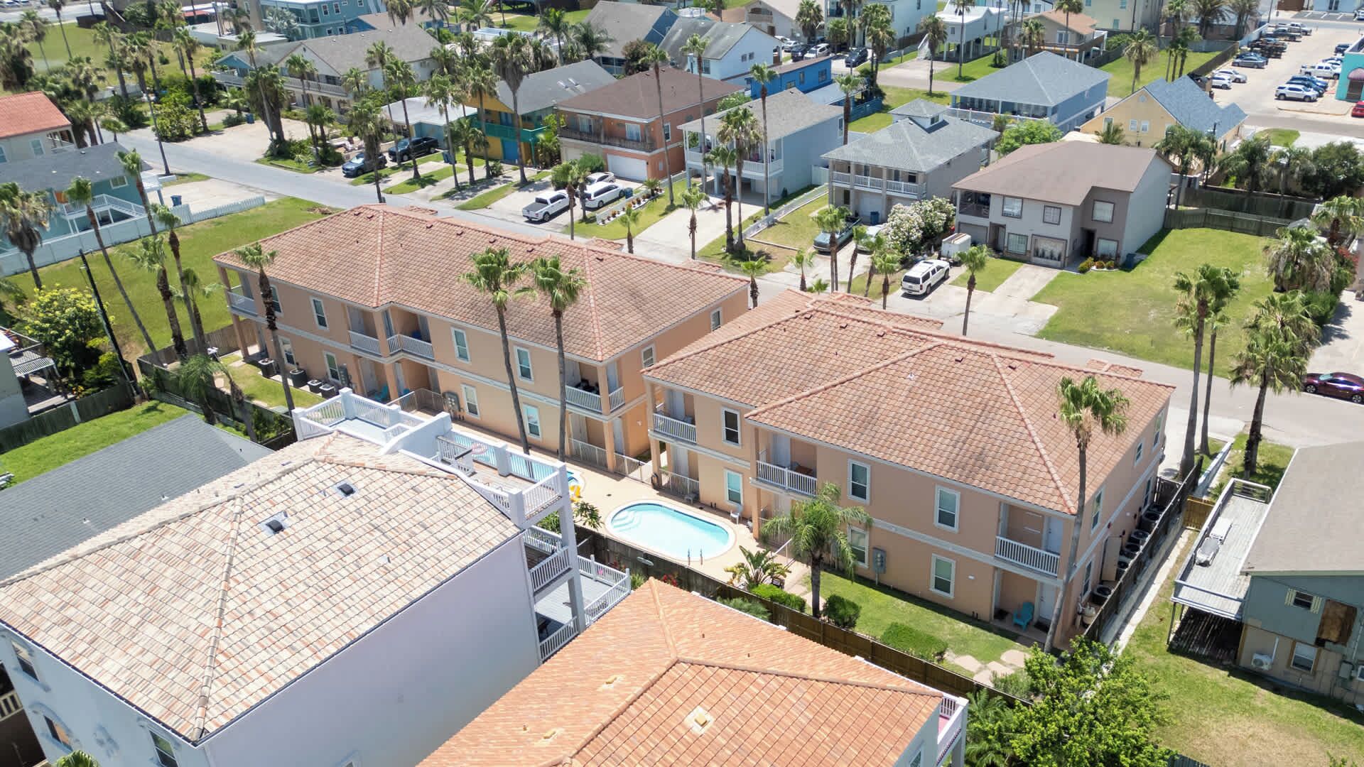 A multi-story building with a swimming pool, surrounded by palm trees and other residential buildings.