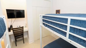 A bunk bed with a blue mattress, a desk with a chair, a television mounted on the wall, and a wardrobe. - 3BR Condo - 9 Beds - Pool - Walk to Beach - SPI (South Padre Island)