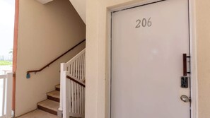 A white door with the number 206, a white staircase with a wooden handrail, and a metal door handle. - 3BR Condo - 9 Beds - Pool - Walk to Beach - SPI (South Padre Island)