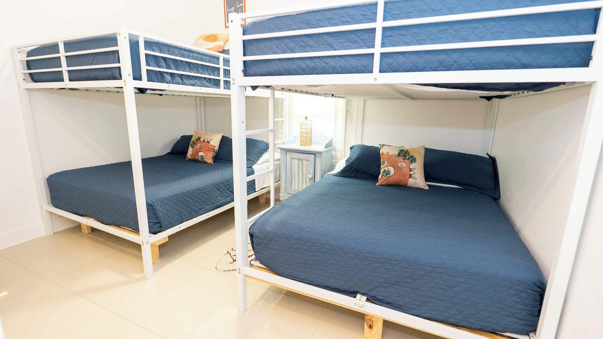 Two bunk beds with blue bedding and pillows, a small table, and a white wall.