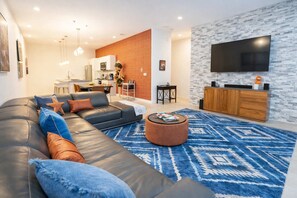 Ein modernes Wohnzimmer mit einer Eckcouch, einem Couchtisch, einem Fernseher und einer Küche im Hintergrund.