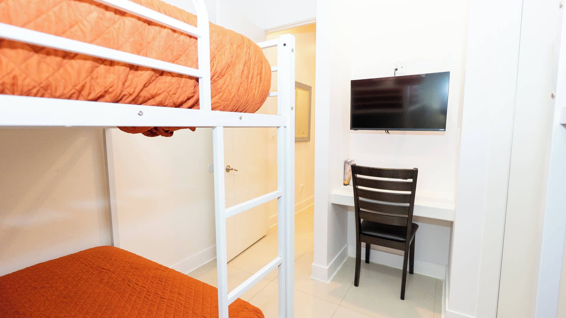 A bunk bed with a desk and chair, a television, and a door.
