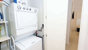 Ett tvättrum med en tvättmaskin och en torktumlare placerade ovanpå varandra, en hylla med rengöringsmedel och en dörr som leder till ett annat rum.