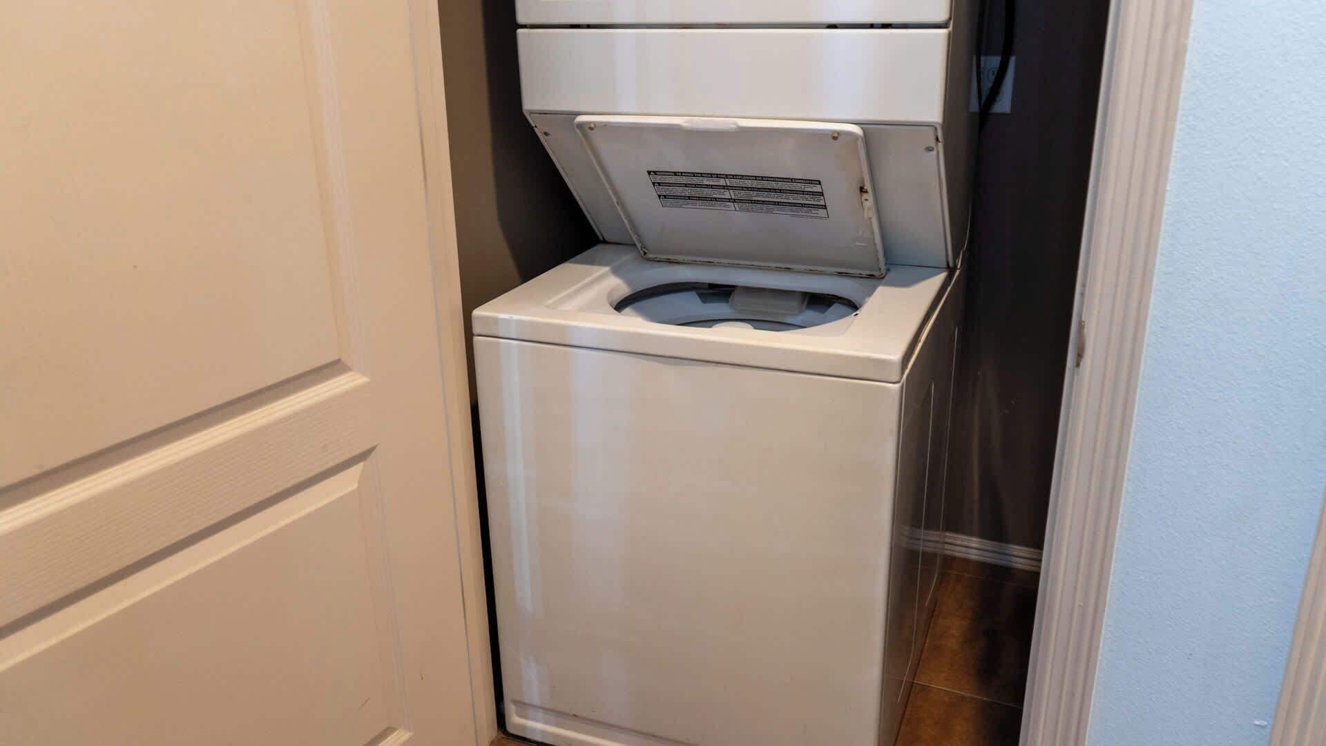A compact, white, front-loading washing machine in a narrow hallway.