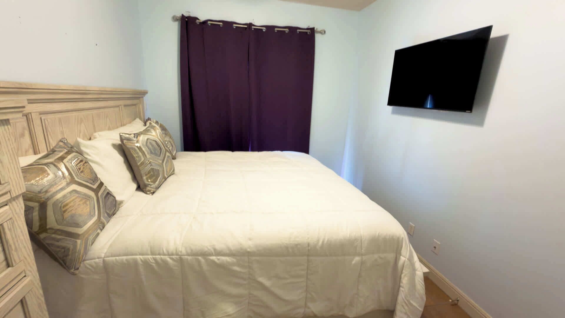 A bedroom with a bed, a TV mounted on the wall, and a purple curtain.