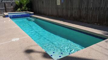 Una piscina rectangular con borde de azulejos, una valla de madera al fondo y agua cristalina de color azul.