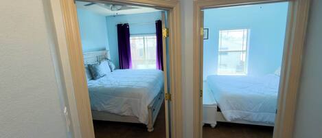 A bedroom with two beds, a window, and a door.