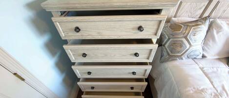 A wooden dresser with multiple drawers and knobs, a remote control on top, and a patterned pillow on the bed.