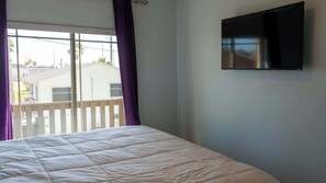 Un dormitori amb un llit, una televisió penjada a la paret i una finestra amb cortines.