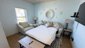 A bedroom with a bed, a sofa, a small table, a lamp, a window, and a wall clock. - Near Beach Retreat - Ground Floor - Pool - Walk to All (South Padre Island)