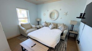 A bedroom with a bed, a sofa, a small table, a lamp, a window, and a wall clock. - Near Beach Retreat - Ground Floor - Pool - Walk to All (South Padre Island)