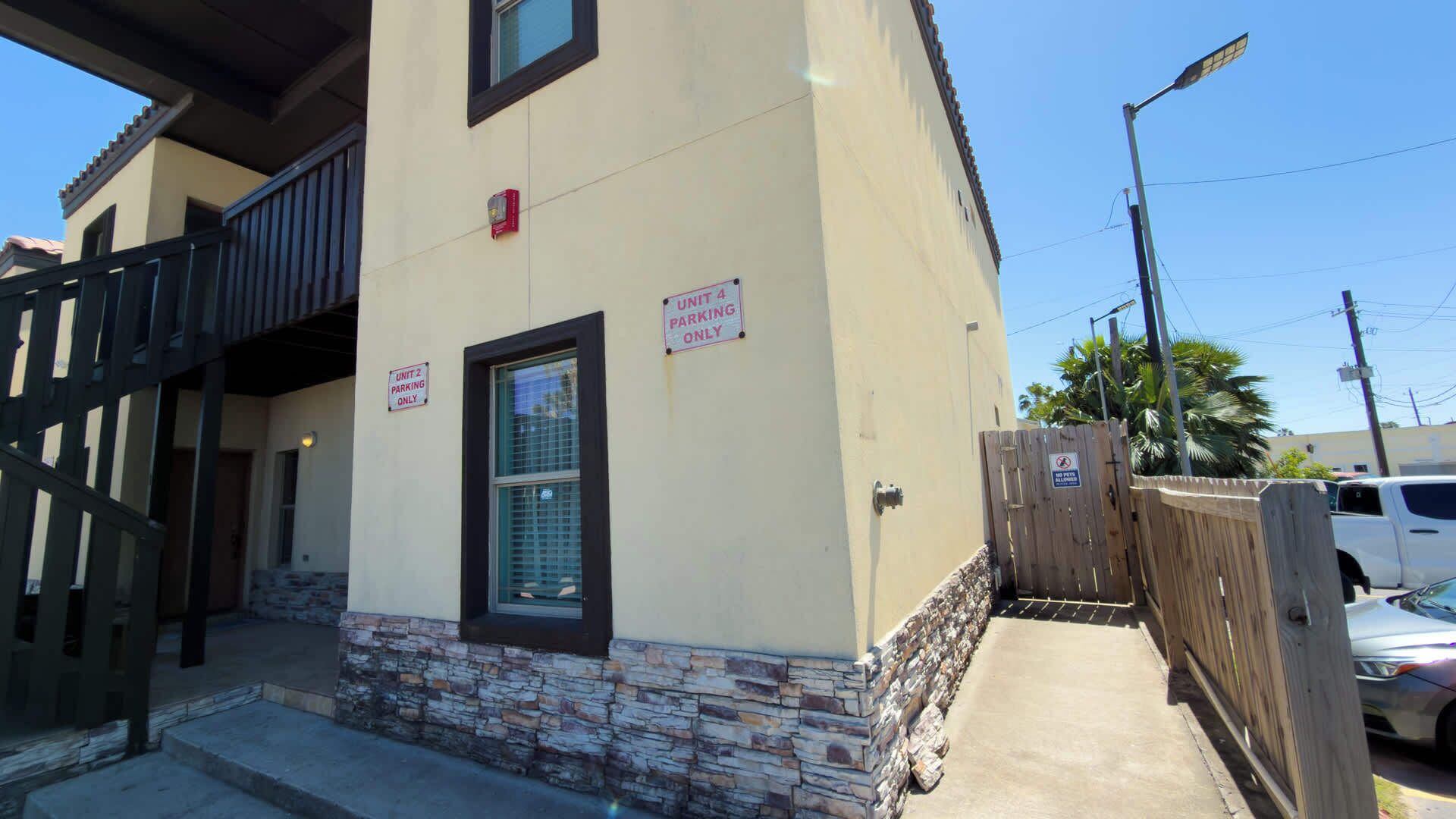 A building with a stone base, two windows, and signs indicating 'Unit 2 Parking Only' and 'Unit 4 Parking Only.'