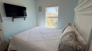 A bedroom with a bed, a TV mounted on the wall, a window, and a door. - Near Beach Retreat - Ground Floor - Pool - Walk to All (South Padre Island)
